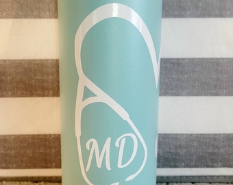 May include: A light teal insulated water bottle with a black handle and lid. A white stethoscope graphic with the letters "MD" is displayed on the front. The bottle is designed for medical professionals.