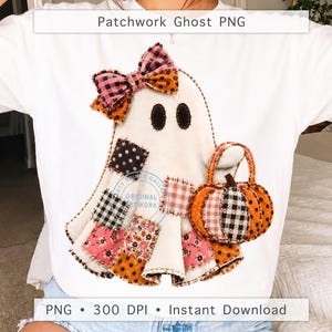 May include: A white t-shirt featuring a graphic of a cream-colored ghost with black stitched eyes, wearing a pink and orange plaid bow. The ghost has various patchwork fabric squares in pink, black, and orange patterns and carries a pumpkin basket.