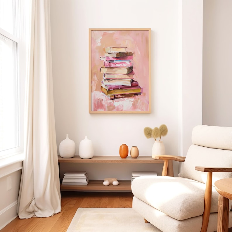 May include: A framed painting of a stack of books in shades of pink, yellow, and brown against a pink background. The painting is hanging on a white wall above a wooden shelf with decorative vases.