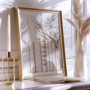 May include: A gold framed picture with a white background and a row of white books with a branch of white flowers in front of them.