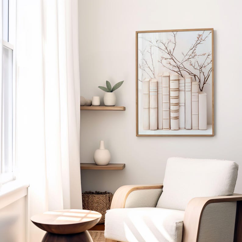 May include: A framed print of a white bookshelf with a row of antique books and a delicate branch of white blossoms. The print is hanging on a white wall in a room with a white armchair and a wooden side table.
