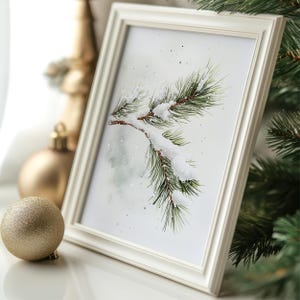 May include: A white frame with a watercolor painting of a pine branch covered in snow. The background is a light blue with white dots.