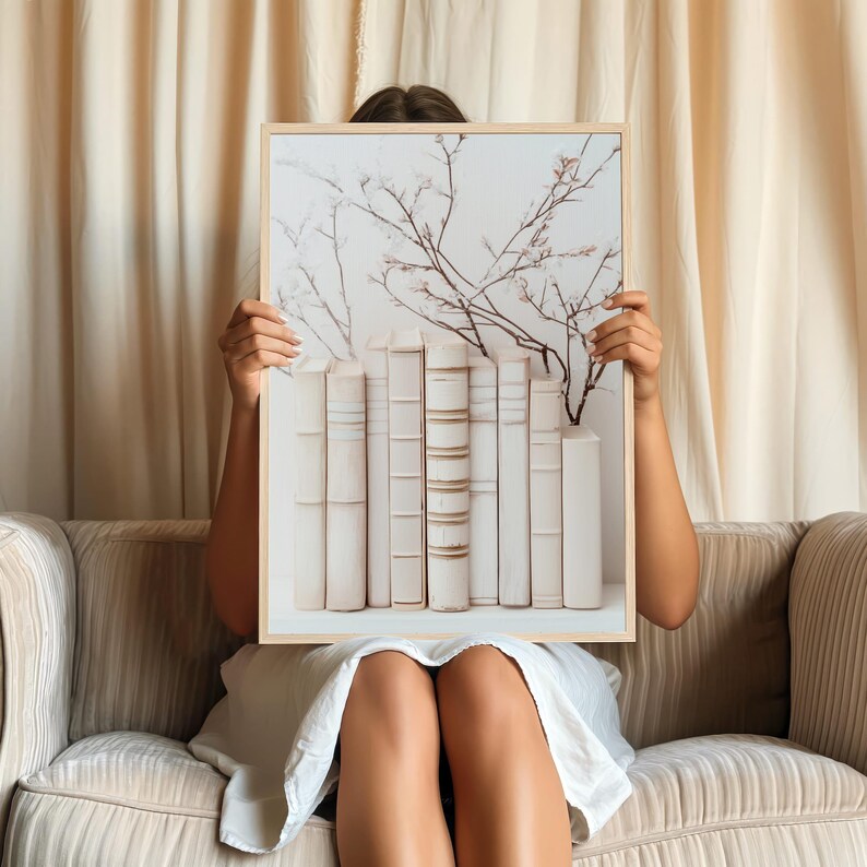 May include: A framed print of a white floral arrangement with a row of white books underneath. The print is held in front of a person's face.