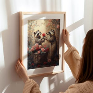 May include: A framed painting of two raccoons in a garden setting. The raccoon on the left is holding a red rose and the raccoon on the right is looking at the rose. The painting is surrounded by a wooden frame.