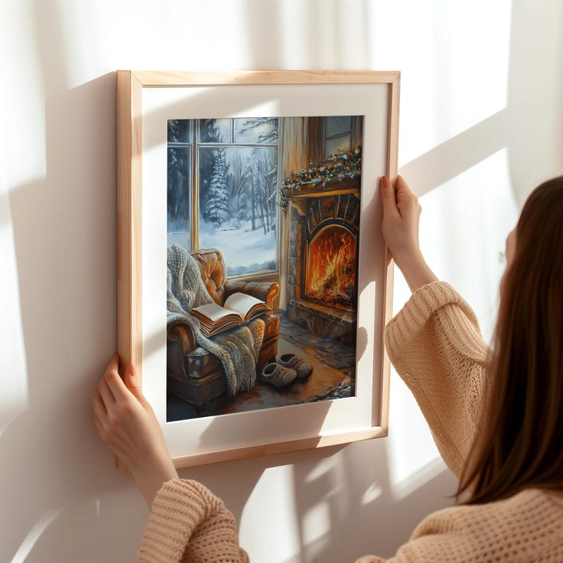 Peut inclure: Une peinture encadr&eacute;e repr&eacute;sentant un salon confortable avec une chemin&eacute;e, une fen&ecirc;tre avec de la neige &agrave; l'ext&eacute;rieur et un fauteuil confortable avec un livre dessus. La peinture est dans un cadre en bois et est accroch&eacute;e &agrave; un mur blanc.