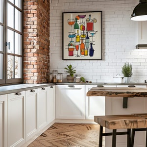 May include: A white kitchen with white cabinets and a brick accent wall. A framed print of colorful line drawings of cocktails and bottles hangs on the wall. A wooden table with a live edge sits in the foreground.