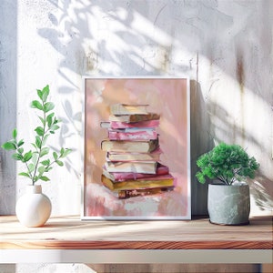 May include: A framed painting of a stack of books in various shades of pink, beige, and brown. The books are arranged in a pyramid shape and are set against a light pink background.