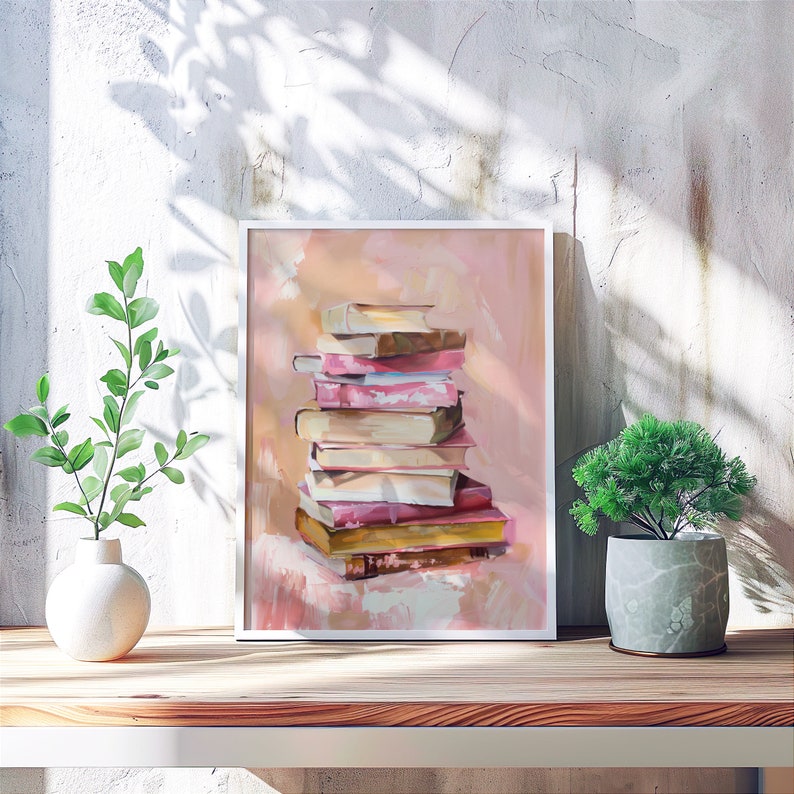 May include: A framed painting of a stack of books in various shades of pink, beige, and brown. The books are arranged in a pyramid shape and are set against a light pink background.