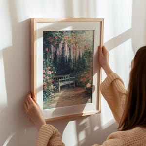 May include: A framed print of a painting depicting a wooden bench in a garden setting. The garden is filled with pink flowers and a trellis of purple wisteria. The bench is surrounded by lush greenery.