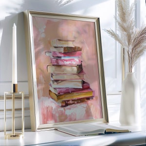 May include: A framed painting of a stack of books in various shades of pink, brown, and yellow. The books are arranged in a stack, with the top book being the smallest and the bottom book being the largest. The painting is set against a light pink background.