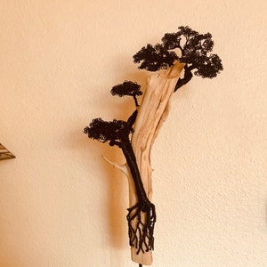 May include: A decorative tree sculpture made from driftwood, with black wire branches and foliage. The trunk and roots are also made of black wire. The sculpture is mounted on a black metal stand, a unique piece of art.