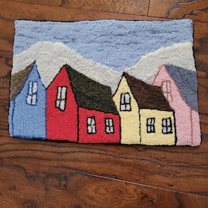 May include: A colorful rug depicting a row of houses with a blue sky and white clouds in the background. The houses are red, yellow, blue, and pink.