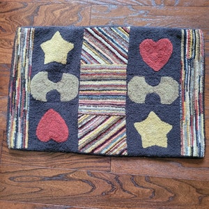 May include: A black and brown striped rug with a patchwork design featuring stars, hearts, and other shapes. The rug is made of a soft, plush material and has a subtle sheen.