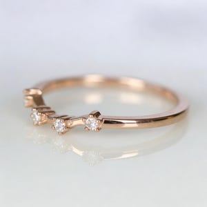 Puede incluir: Anillo de banda de oro rosa con tres peque&ntilde;as piedras preciosas transparentes. El anillo tiene un dise&ntilde;o delicado y curvado. Las piedras preciosas est&aacute;n espaciadas uniformemente a lo largo de la parte superior de la banda.