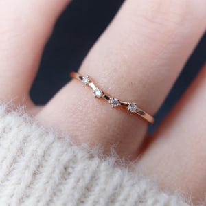 Puede incluir: Un delicado anillo de oro rosa con un dise&ntilde;o curvo. El anillo presenta cinco peque&ntilde;os diamantes brillantes engastados a lo largo de la curva. El anillo se muestra en un dedo, destacando su estilo elegante y minimalista.