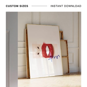 May include: A framed print of a close-up of a pair of red lips with a blue signature in the bottom right corner. The print is leaning against a white wall with wood paneling.