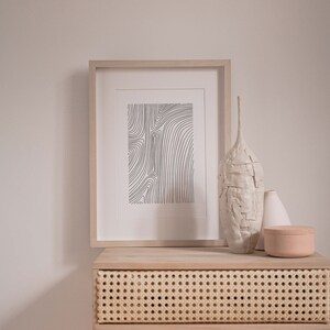 K&ouml;nnte beinhalten: Ein Holz-Beistelltisch mit einer Schublade aus geflochtenem Rattan, einem gerahmten Schwarz-Wei&szlig;-Linienkunst-Druck, einer wei&szlig;en Keramikvase, einer wei&szlig;en Keramikvase und einer hellbraunen Keramikdose.