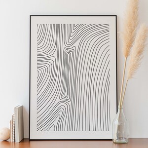 K&ouml;nnte beinhalten: Ein schwarzer gerahmter Druck mit wei&szlig;em Hintergrund und einem abstrakten Linienmuster in Schwarzwei&szlig;. Der Druck h&auml;ngt an einer wei&szlig;en Wand &uuml;ber einer Kommode aus Holz mit zwei Schubladen.