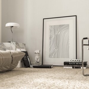 K&ouml;nnte beinhalten: Ein Schwarz-Wei&szlig;-Druck mit abstrakter Linienkunst in einem schwarzen Rahmen, der an einer wei&szlig;en Wand h&auml;ngt. Der Druck ist von B&uuml;chern und einer wei&szlig;en Lampe auf einem Marmortisch umgeben.