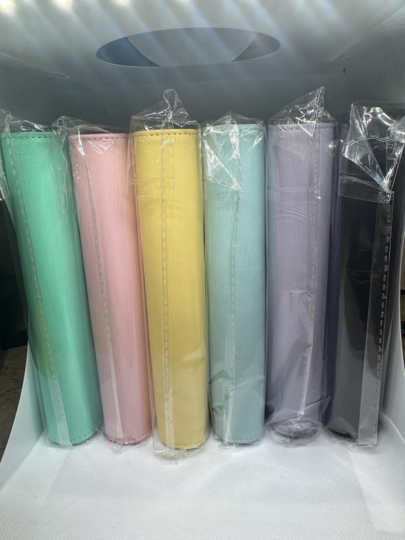 May include: A collection of colorful, cylindrical items wrapped in clear plastic. The items are in shades of mint green, pink, yellow, light blue, lavender, and black. The items appear to be made of a soft material.