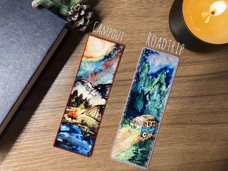 K&ouml;nnte beinhalten: Zwei Aquarell-Lesezeichen mit Camping-Motiv. Das Lesezeichen "Campout" zeigt einen sternenklaren Nachthimmel, Berge, ein Lagerfeuer und ein Zelt. Das Lesezeichen "Roadtrip" zeigt einen sternenklaren Nachthimmel, B&auml;ume und einen blauen Van.