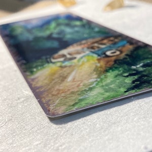 K&ouml;nnte beinhalten: Ein Aquarellbild eines alten Lieferwagens, der eine kurvenreiche Stra&szlig;e durch einen &uuml;ppigen gr&uuml;nen Wald f&auml;hrt. Der Lieferwagen ist in Blaut&ouml;nen und Wei&szlig; mit einem gelben Streifen an der Seite bemalt. Der Wald ist in Gr&uuml;nt&ouml;nen mit einigen B&auml;umen im Hintergrund bemalt. Die Stra&szlig;e ist in Braunt&ouml;nen und Gelb mit einigen wei&szlig;en Linien bemalt.