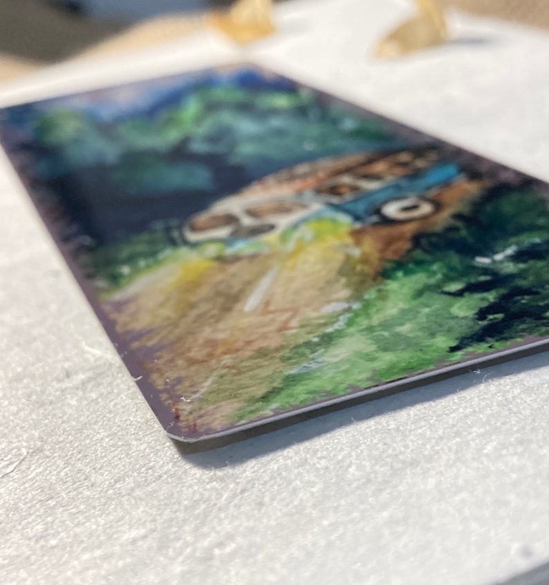 K&ouml;nnte beinhalten: Ein Aquarellbild eines alten Lieferwagens, der eine kurvenreiche Stra&szlig;e durch einen &uuml;ppigen gr&uuml;nen Wald f&auml;hrt. Der Lieferwagen ist in Blaut&ouml;nen und Wei&szlig; mit einem gelben Streifen an der Seite bemalt. Der Wald ist in Gr&uuml;nt&ouml;nen mit einigen B&auml;umen im Hintergrund bemalt. Die Stra&szlig;e ist in Braunt&ouml;nen und Gelb mit einigen wei&szlig;en Linien bemalt.