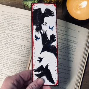 May include: A bookmark featuring a watercolor illustration of three black crows flying against a starry night sky. The bookmark is a close-up of the illustration and includes a red border.