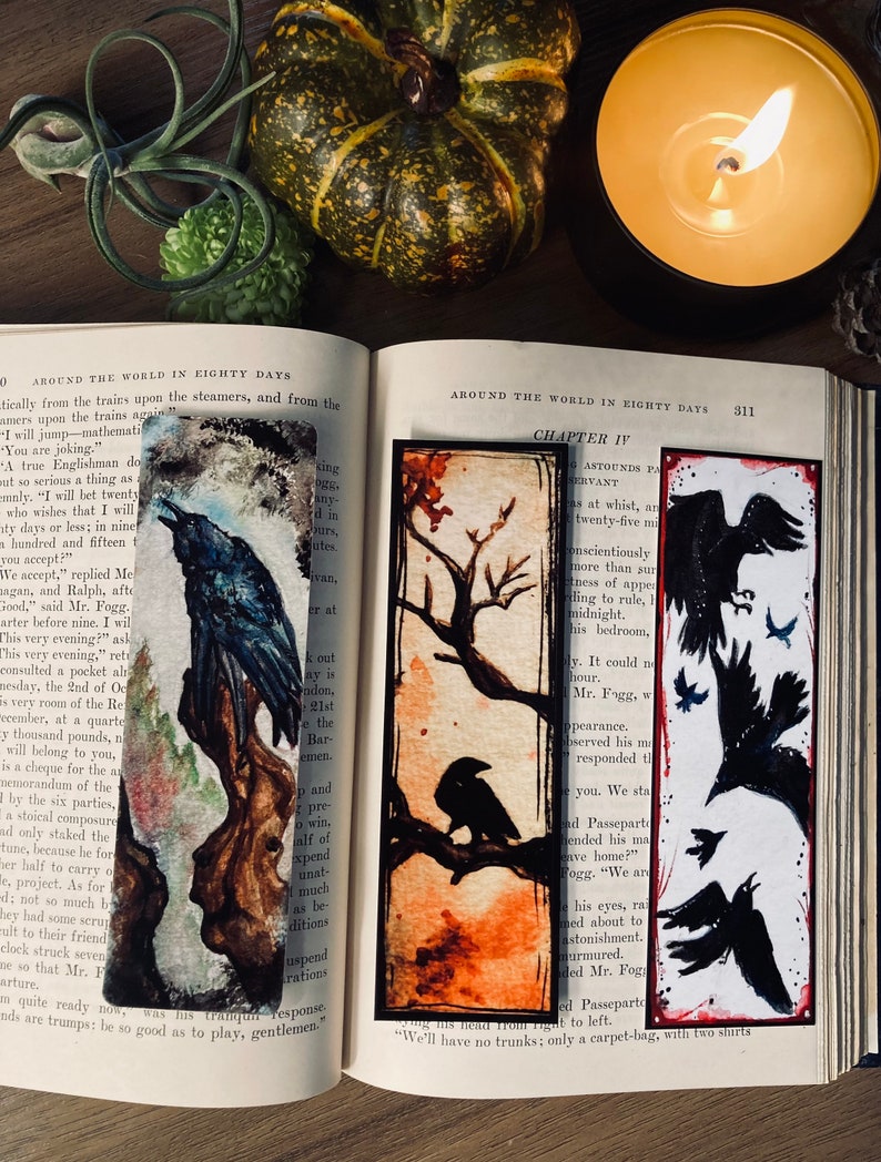 May include: A vintage book with a black raven illustration on the cover. The book is open to a page with the title "Around the World in Eighty Days" and a chapter titled "Chapter IV". The page also features a black and white illustration of a raven on a branch.