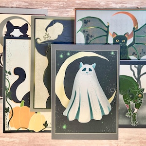 Peut inclure: Une collection d'estampes d'art sur le thème d'Halloween avec des chats, des chauves-souris et des citrouilles. Les estampes présentent une variété de motifs, dont un squelette de chat, une sorcière, un chat fantôme sur un croissant de lune et une chauve-souris.