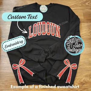 May include: A black crewneck sweatshirt featuring the red glitter text LOUDOUN in an arched collegiate font across the chest. Two red glitter bow graphics are positioned near the bottom hem. The garment includes a circular logo tag at the neck.