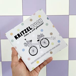 May include: A white booklet with colorful polka dots and the text "KRITZELBUCH" in black. The text "Hurra, es wird geheiratet!" is also in black. The booklet features a black and white illustration of a bicycle with flowers in a basket. The text "ZUM KRITZELN, KREATIV SEIN UND SPA&szlig; HABEN" is in black.