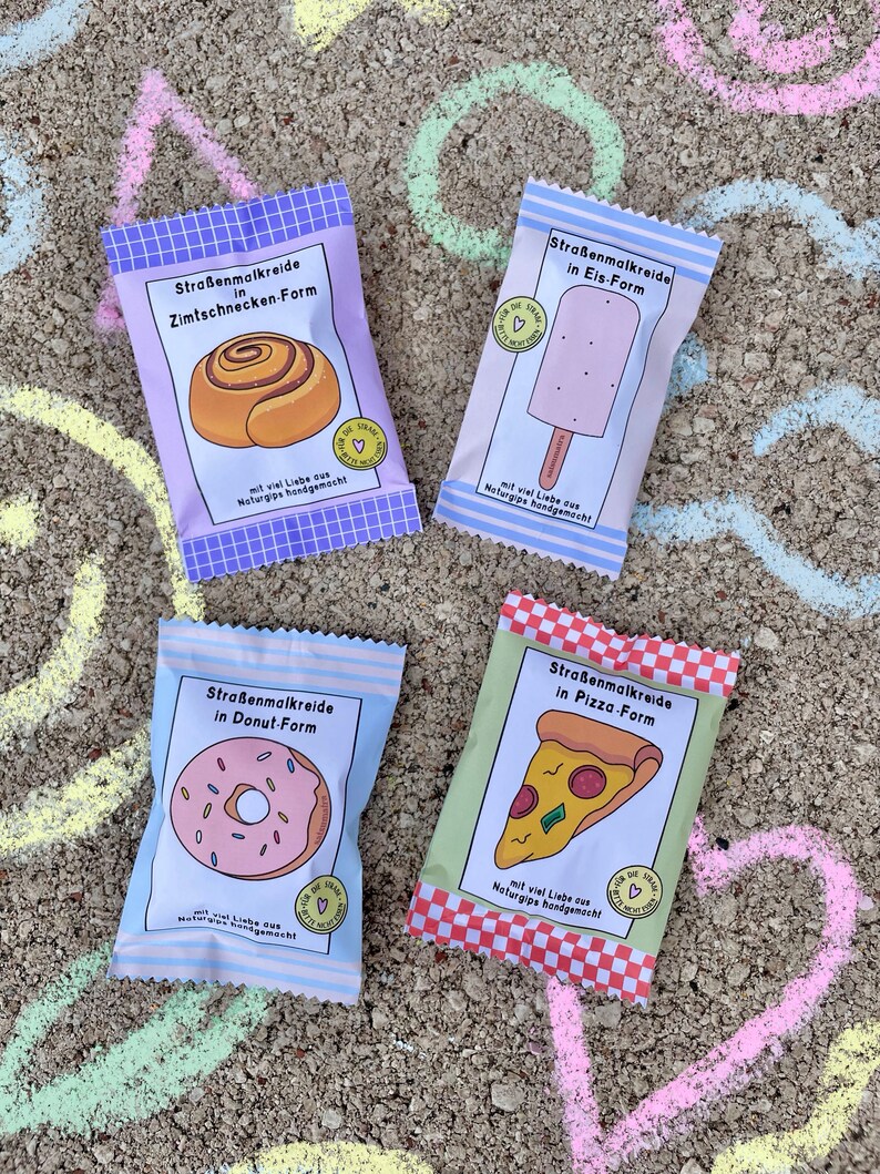 May include: Four colorful packages of sidewalk chalk shaped like different foods. The packages are labeled "Stra&szlig;enmalkreide" which is German for sidewalk chalk. The food shapes are a cinnamon roll, a popsicle, a donut, and a pizza.