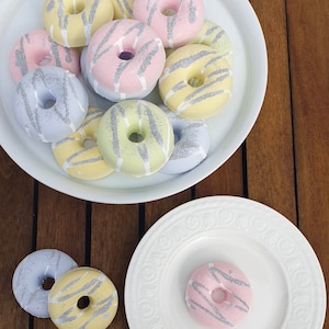 May include: A white plate with a variety of pastel-colored donuts with silver glitter. The donuts are arranged in a circle with the silver glitter facing up. The donuts are on a wooden table.