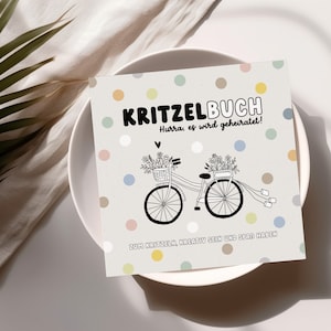 May include: A white card with a colorful polka dot pattern. The card has black text that reads "KRITZELBUCH Hurra, es wird geheiratet!" and "ZUM KRITZELN, KREATIV SEIN UND SPAR HABEN". There is a black and white illustration of a bicycle with flowers in baskets on the handlebars.
