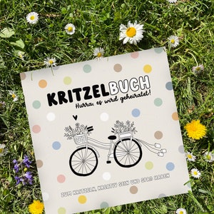 May include: A white card with colorful polka dots and the text "KRITZELBUCH Hurra, es wird geheiratet!"  A black and white illustration of two bicycles with flowers in baskets and streamers attached to the handlebars. The text "ZUM KRITZELN, KREATIV SEIN UND SPAR HABEN" is at the bottom of the card.