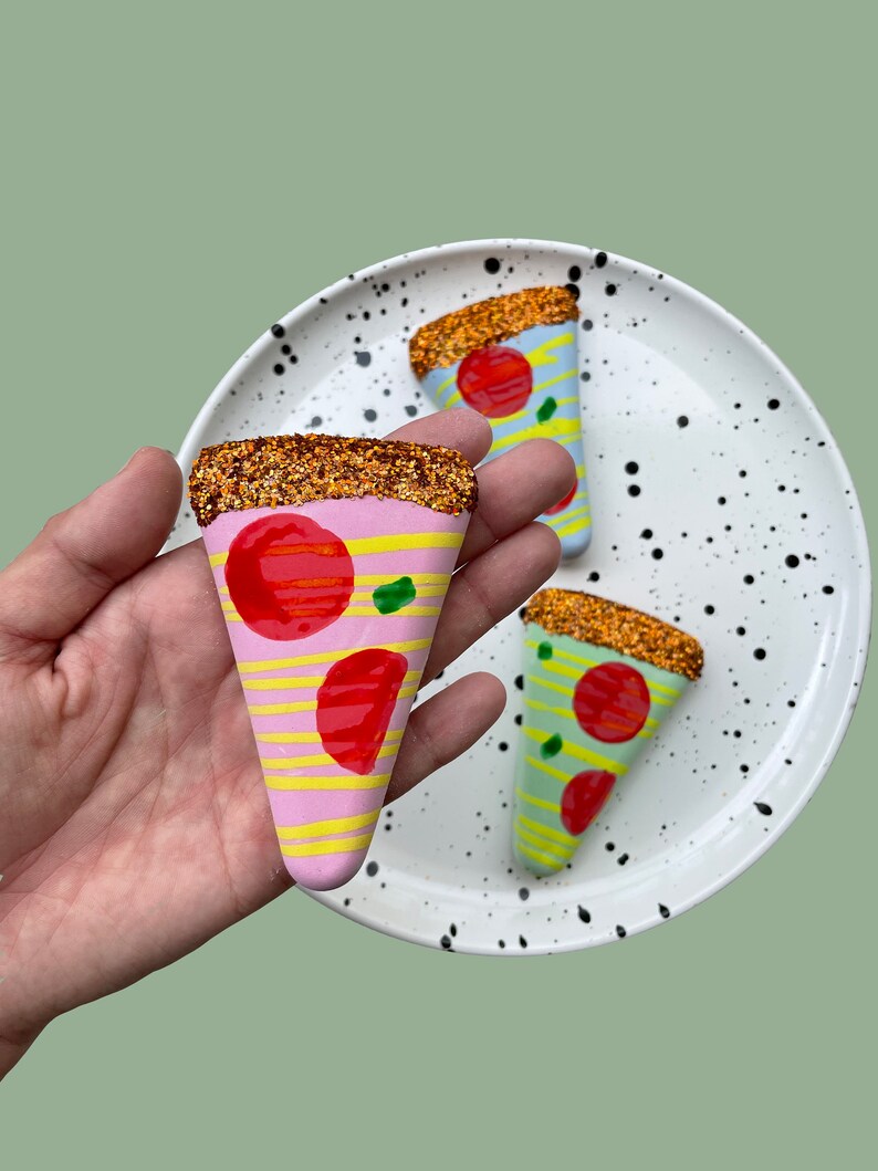 Op de afbeelding: Drie keramische pizza-puntversieringen met glitteraccenten. De punten zijn roze, blauw en groen met rode en gele toppings.