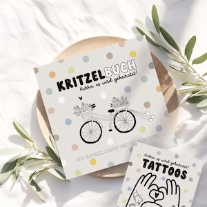 May include: A white card with a black and white illustration of a bicycle with flowers in the basket. The text on the card reads "Kritzelbuch Hurra, es wird geheiratet! Zum Kritzeln, kreativ sein und Spa&szlig; haben".