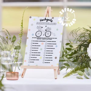 May include: A white card with a black and white illustration of a bicycle with flowers on the handlebars. The card has a checklist with the title "Hochzeits Schnitzeljagd" and a list of items to find at a wedding, such as a bouquet, a camera, a piece of cake, a blue dress, a ring, and a heart.