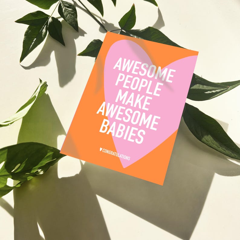 May include: A greeting card with an orange background and a pink heart shape. The card reads "AWESOME PEOPLE MAKE AWESOME BABIES" in white text. The word "Congratulations" is at the bottom. Green leaves are in the background.
