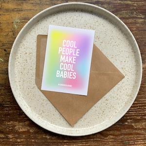 May include: A card with a rainbow gradient background and the text "Cool People Make Cool Babies" in white. The card has a small "Congratulations" printed at the bottom.