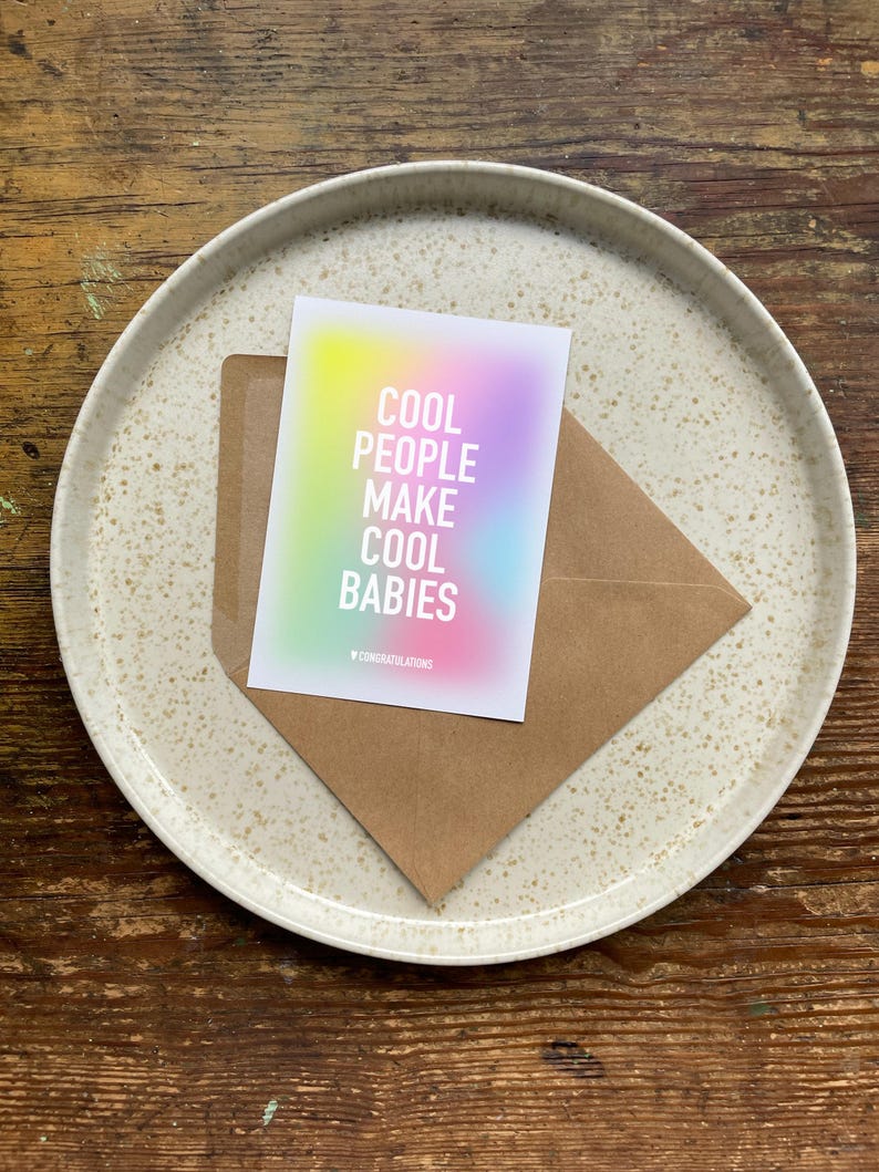 May include: A card with a rainbow gradient background and the text "Cool People Make Cool Babies" in white. The card has a small "Congratulations" printed at the bottom.