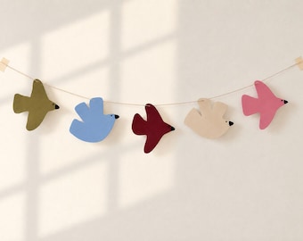 Può includere: Una ghirlanda decorativa con cinque sagome piatte a forma di uccello nei colori verde oliva, azzurro, rosso scuro, beige e rosa. Ogni uccello presenta un piccolo punto nero per l'occhio e un becco nero, appesi a un filo sottile.