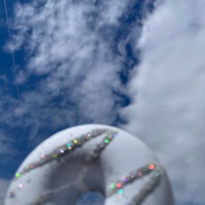 May include: A white donut with silver glitter sprinkles against a blue sky with white clouds.