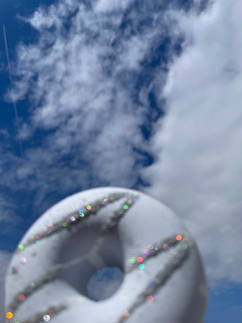 May include: A white donut with silver glitter sprinkles against a blue sky with white clouds.
