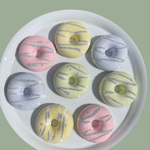 May include: A set of seven pastel-colored donuts with silver glitter frosting and sprinkles. The donuts are arranged in a circle on a white plate.