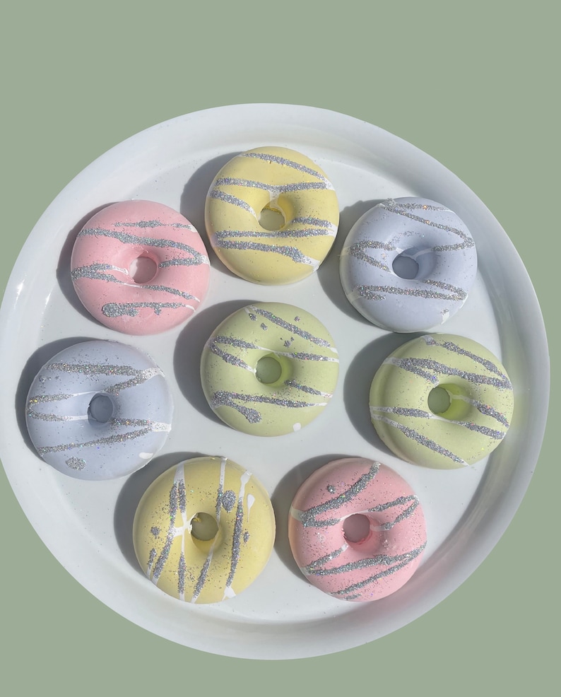May include: A set of seven pastel-colored donuts with silver glitter frosting and sprinkles. The donuts are arranged in a circle on a white plate.