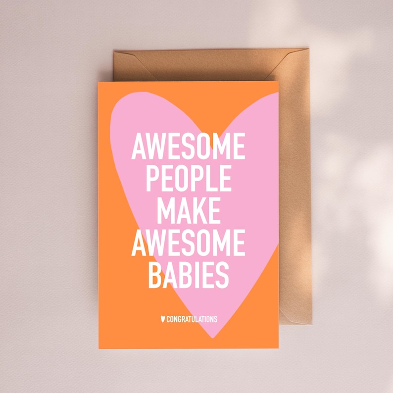 May include: A greeting card with the text "AWESOME PEOPLE MAKE AWESOME BABIES" in white on a pink heart shape, set against an orange background. The card includes a brown envelope and the word "CONGRATULATIONS" at the bottom.