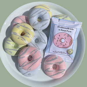 May include: A set of colorful donut-shaped sidewalk chalk in a variety of pastel colors with silver glitter. The chalk is packaged in a clear plastic bag with a label that reads "Stra&szlig;enmalkreide in Donut-Form" and "mit viel Liebe aus Naturgips handgemacht".