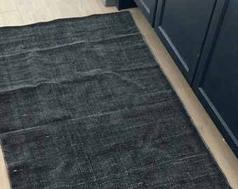May include: A dark gray area rug with a woven texture. The rug is laid out on a light wood floor.